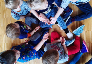 Dzieci siedzą na podłodze i pokazują rączki z pieczątką wirusa.